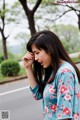 A woman in a blue floral shirt standing on the side of a road.