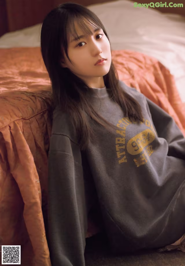A woman sitting on a bed wearing a sweatshirt.