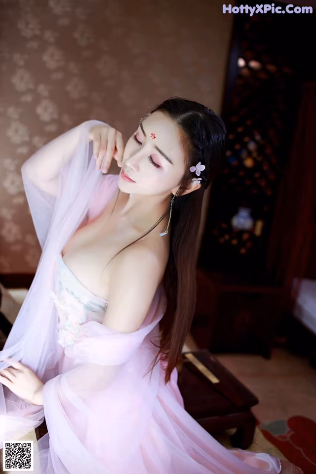 A woman in a pink dress sitting on a bed.