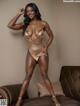 A woman in a gold bodysuit posing on a brown couch.