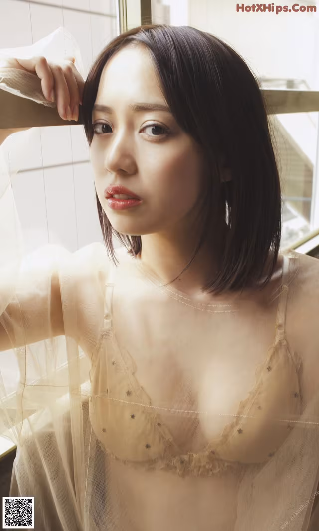 A woman in a sheer lingerie leaning against a window.