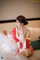 A woman in a red and white kimono sitting on a bed.