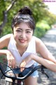 A woman sitting on a bike smiling at the camera.