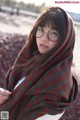 A woman wearing glasses and a plaid blanket on a beach.