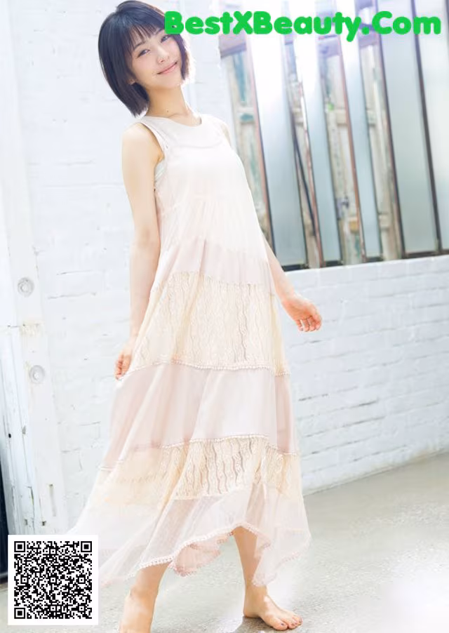 A woman in a pink dress standing in front of a white brick wall.