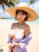 A woman in a purple dress and a straw hat on the beach.