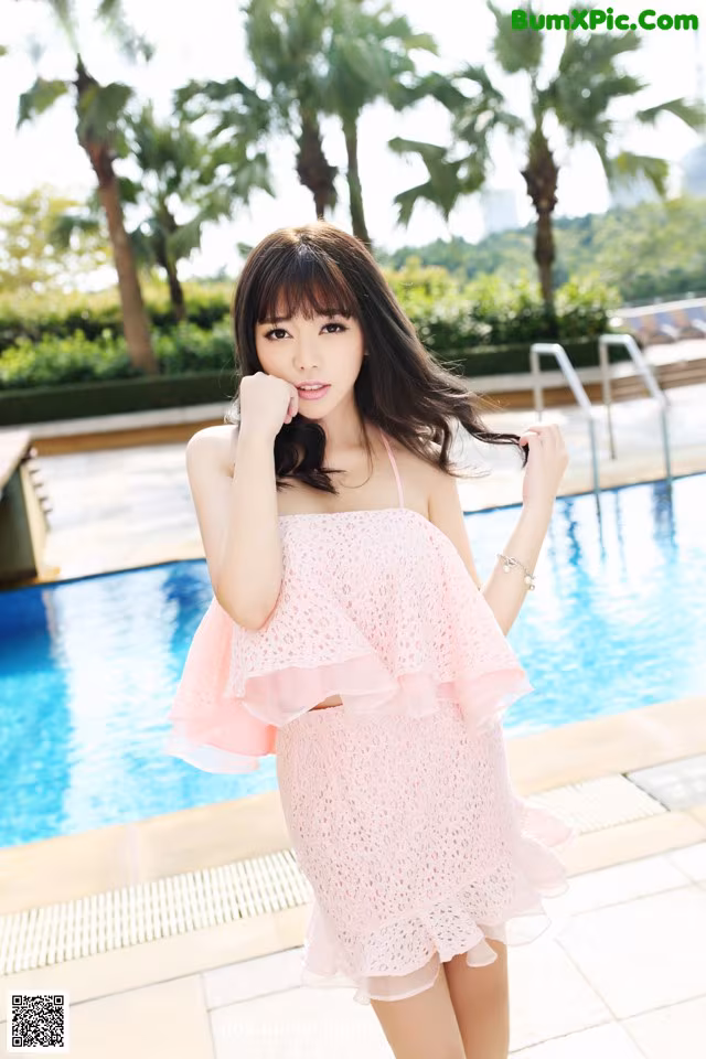A woman in a pink dress standing next to a swimming pool.