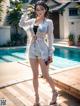 A woman standing next to a swimming pool wearing a white shirt and shorts.