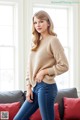 A woman in a beige sweater and jeans posing on a couch.