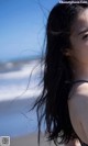 A woman with long black hair standing on a beach.