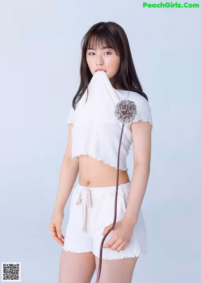 A woman in a white top and shorts holding a flower.