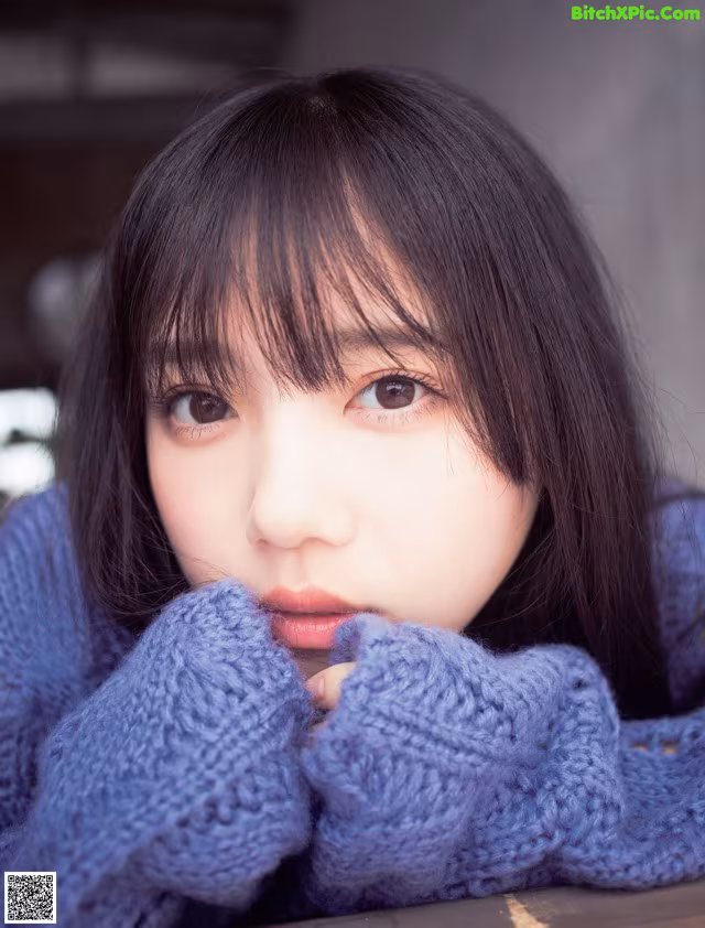 A woman with long black hair wearing a blue sweater.
