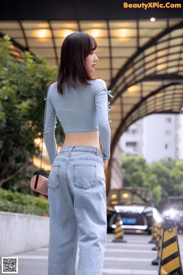 A woman in a blue top and jeans standing on a sidewalk.