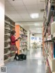 A woman in a school uniform is reading a book in a library.